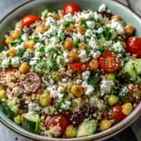 Tossing the fluffy quinoa, chickpeas, and fresh herbs with a zesty lemon vinaigrette dressing in a large bowl.
