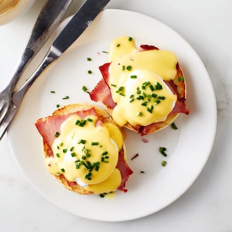 Golden poached Eggs Benedict with creamy hollandaise on toasted English muffins and Canadian bacon.