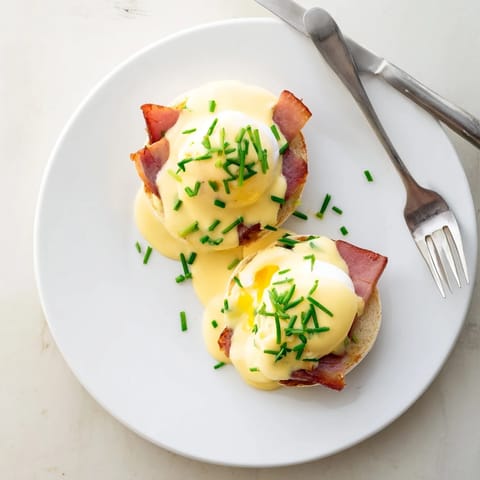 Eggs Benedict served hot with rich hollandaise and chopped chives on a brunch plate.