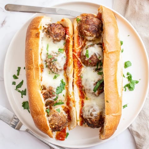 Melted provolone cheese stretches over a hearty Meatball Sub, served hot with fresh parsley garnish.
