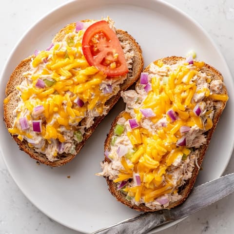 A classic tuna melt sandwich with creamy tuna salad, bubbling cheese, and a side of crisp dill pickles.
