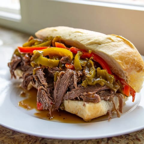 Overhead view of a juicy Italian Beef Sandwich on a toasted roll piled with savory beef and colorful giardiniera, served with a small bowl of au jus.