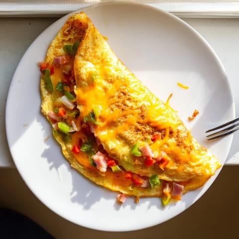 Denver Omelet folded with savory ham, peppers, onions, and gooey cheddar, perfect for a classic American breakfast.
