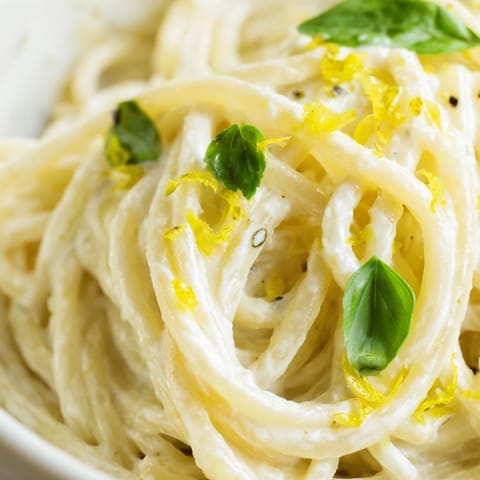 A close-up of lemon ricotta pasta topped with fresh parsley, lemon zest, and a crack of black pepper.