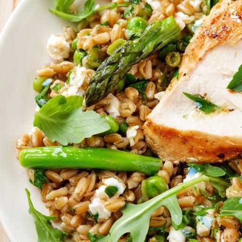 Freshly tossed Warm Spring Farro Chicken Salad served in a white bowl, topped with crumbled feta and herbs, ready for a light lunch.