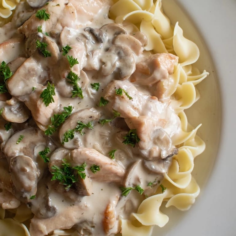A close-up of creamy Chicken and Mushroom Stroganoff with tender chicken, earthy mushrooms, and fresh parsley garnish served atop buttery egg noodles.