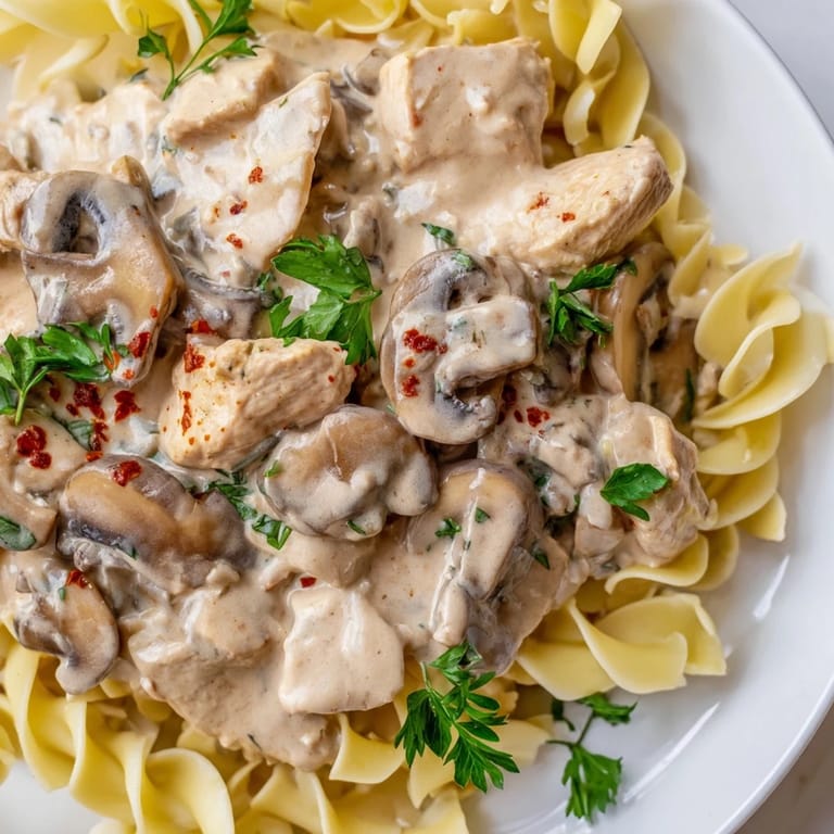 Savory Chicken and Mushroom Stroganoff featuring juicy chicken, sautéed mushrooms, and a rich sour cream sauce served over steaming egg noodles.