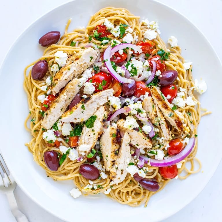 A close-up view of Greek Chicken Spaghetti plated for dinner, highlighting golden chicken, melted feta, and colorful vegetables, ready to be enjoyed with a glass of white wine.