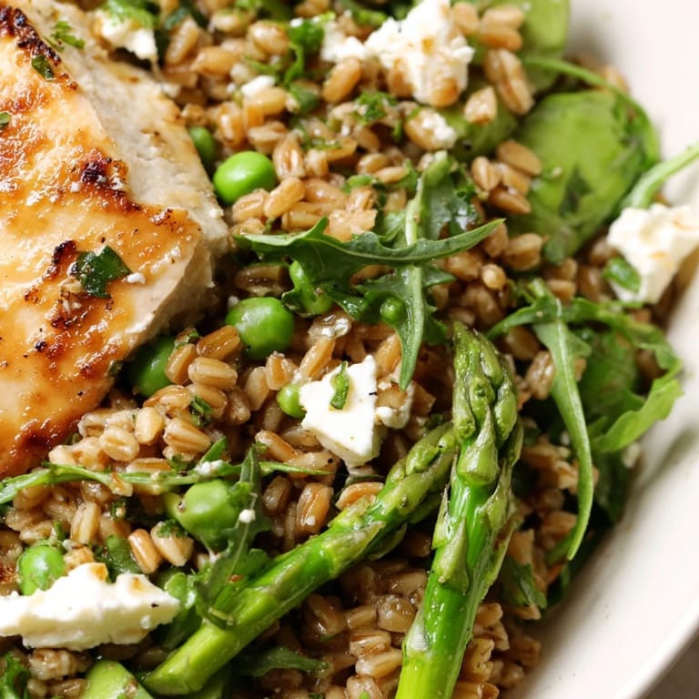 Warm Spring Farro Chicken Salad plated with vibrant green vegetables, golden farro, and sliced chicken drizzled with a glossy lemon vinaigrette.