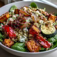 A warm salad bowl featuring roasted sweet potato and zucchini, wilted spinach, and quinoa with a vibrant vinaigrette.
