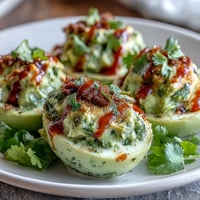 Creamy avocado deviled eggs with a spicy Sriracha drizzle, garnished with fresh cilantro and paprika.